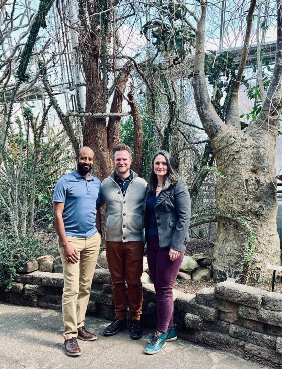 Three people standing shoulder to shoulder smiling at the camera.